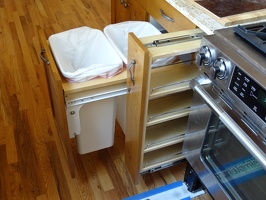 The trash bins and spice rack next to oven